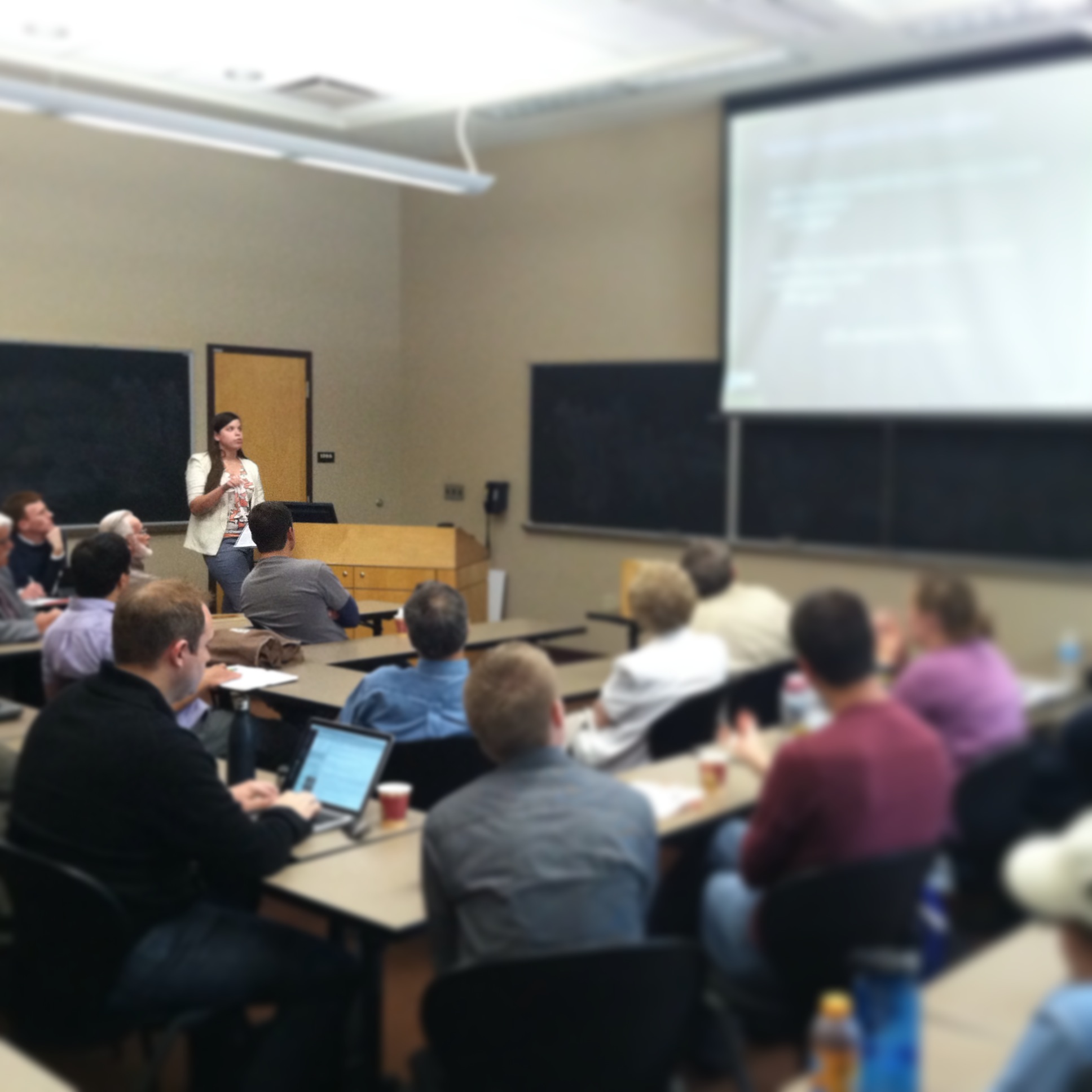 Student Brooke Strayer stands at a podium to deliver a talk to a room full of people